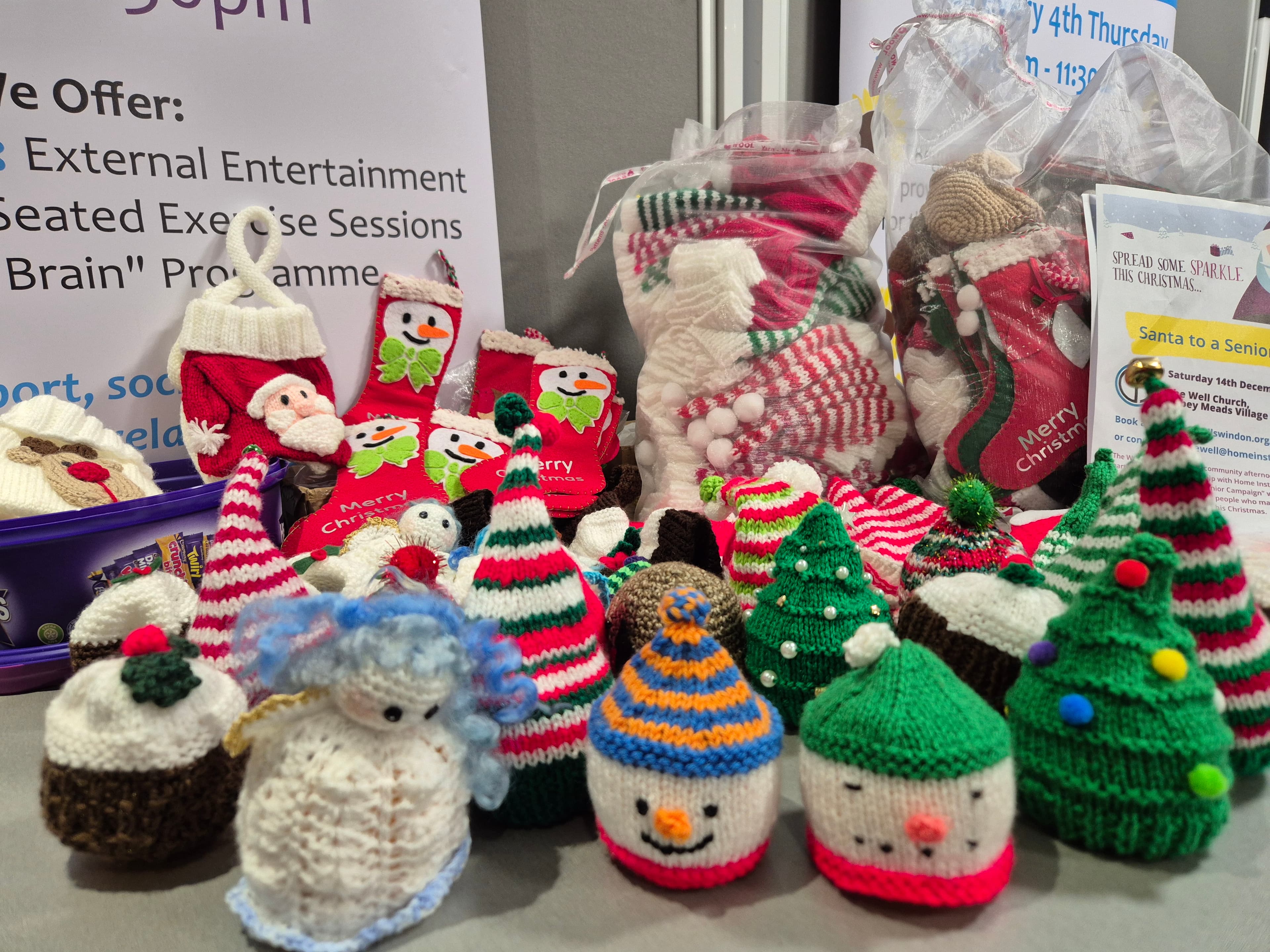 A display of knitted Christmas decorations, including hats, snowmen, trees, and stockings. - Home Instead