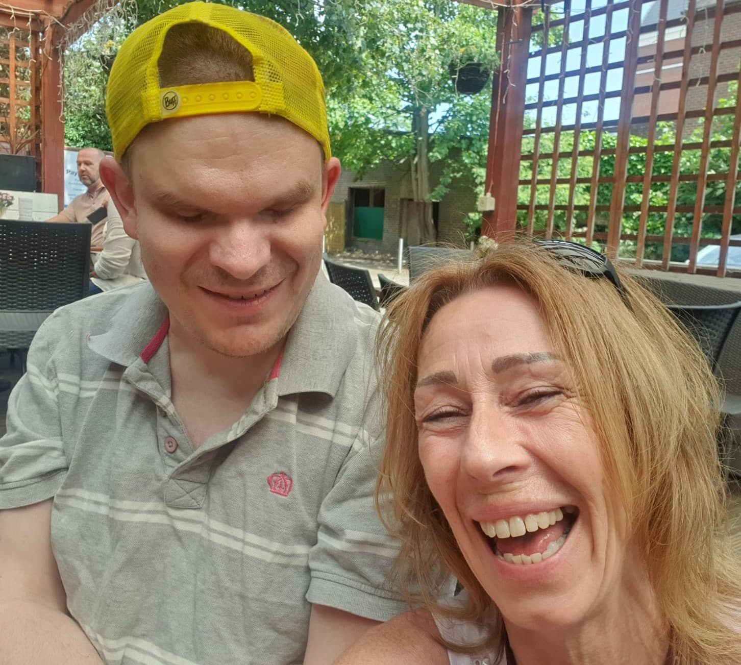 Two people smiling outdoors; a man in a yellow cap and a woman with light brown hair enjoying a sunny day. - Home Instead