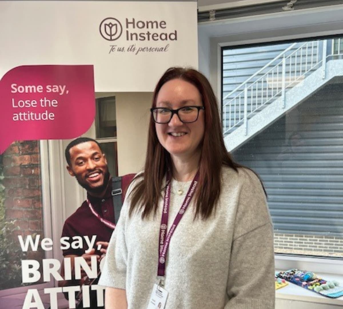 woman with long hair and wearing eyeglasses happy and smiling with a Home Instead banner at the background