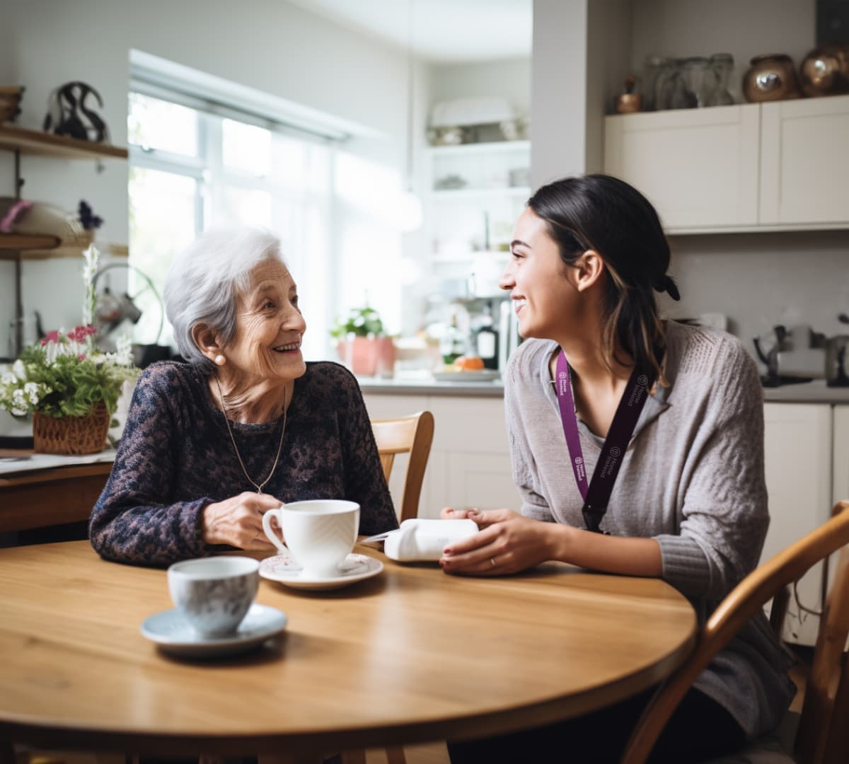 An older woman with grey hair and brown coat happy and smiling with her younger carer holding a coffee both happy and smiling inside the coffee shop