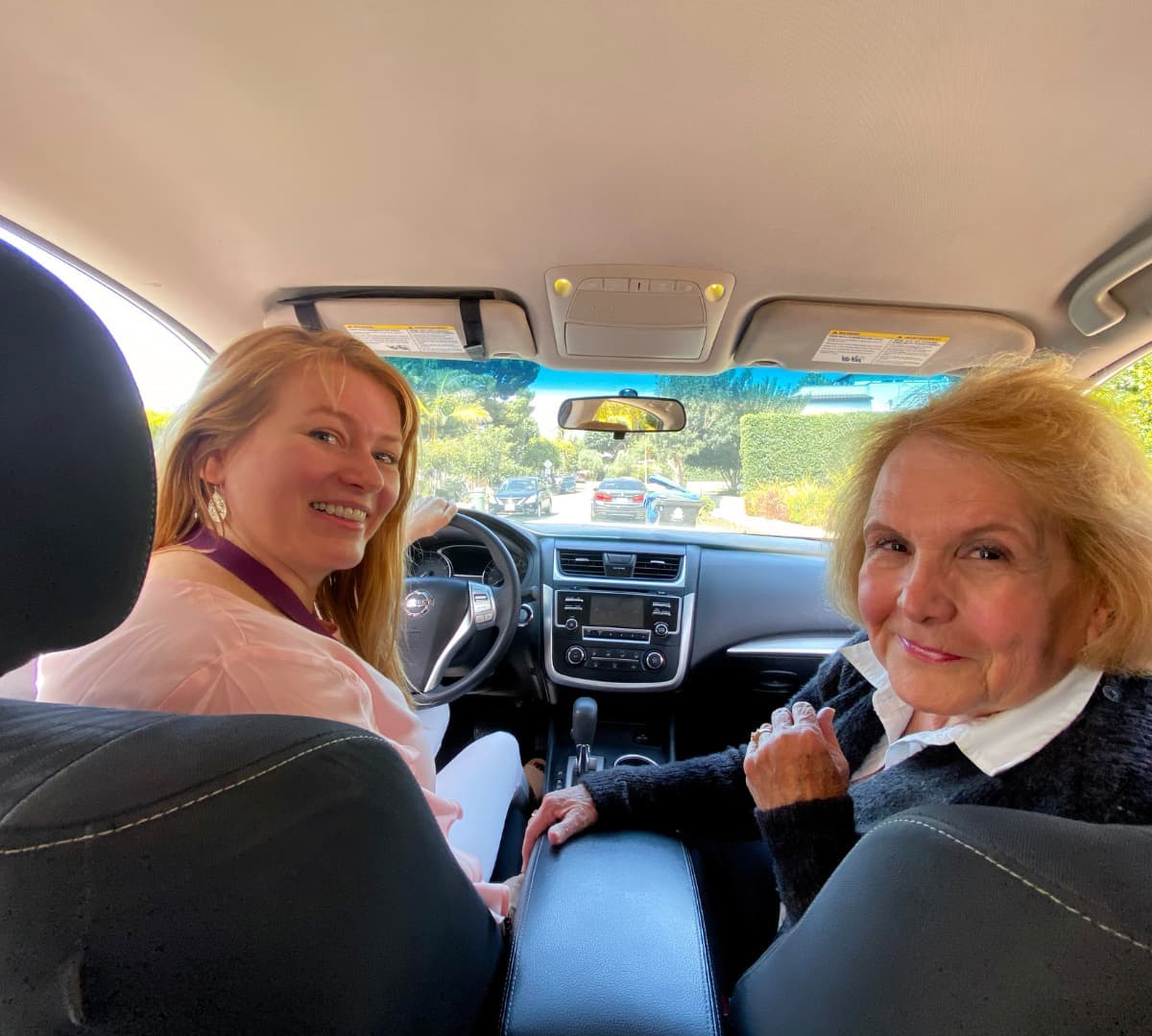 An older woman with her younger female carer both happy and smiling while inside the car