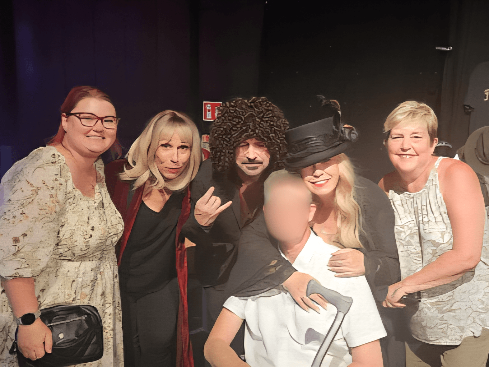 A group of six adults, some in costumes, posing and smiling together indoors at an event. - Home Instead