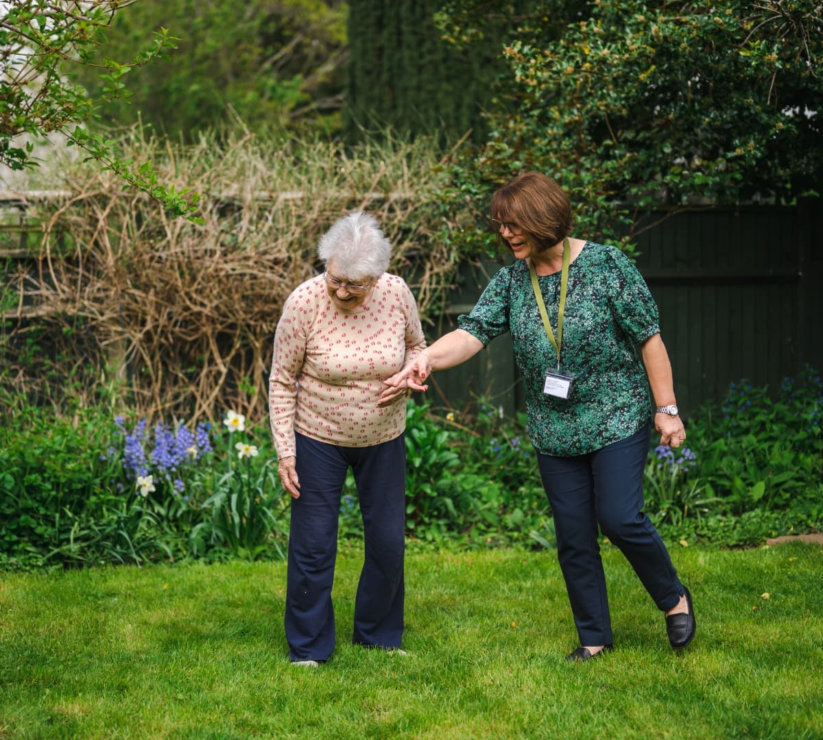 Two women having fun in the garden and surrounded by plants and green grass