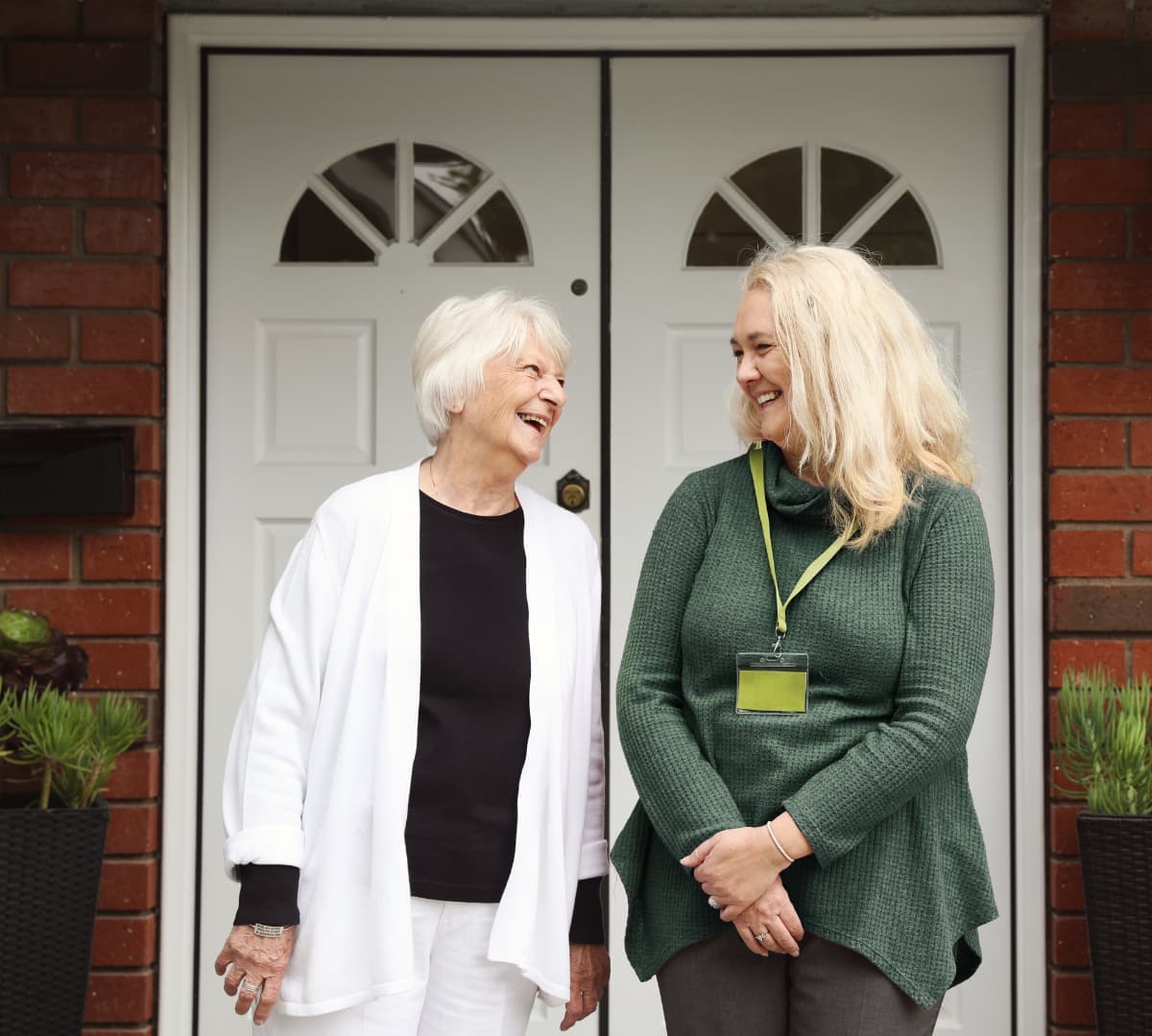 Two women smiling and happy standing together at the front door of the house