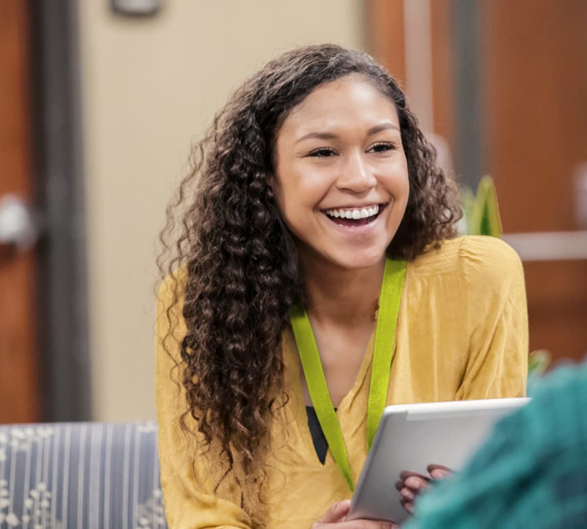 Woman with long curly hair happy and smiling and wearing yellow shirt while speaking to someone
