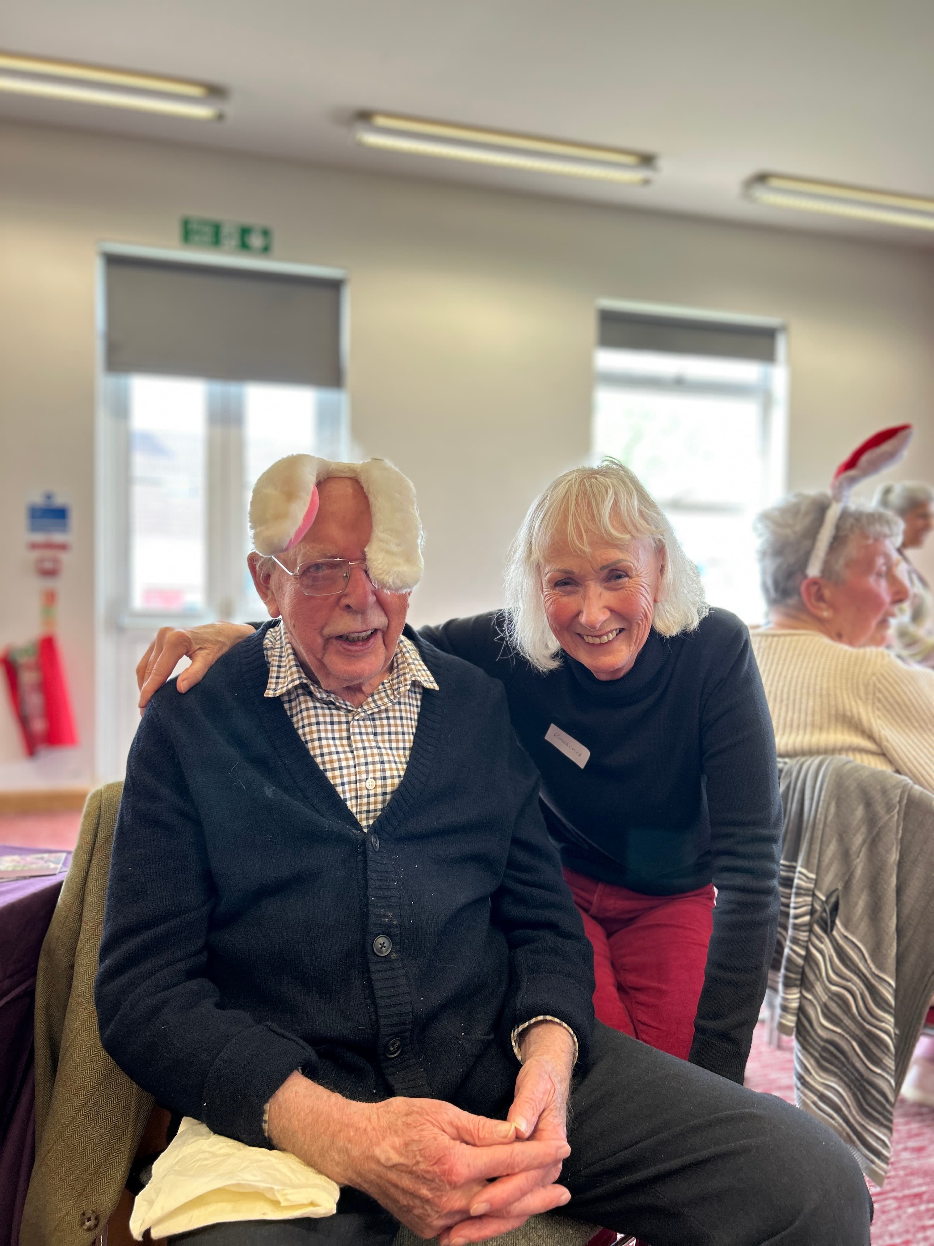 Elderly man and lady at an event, with man wearing rabbit ears celebrating Easter