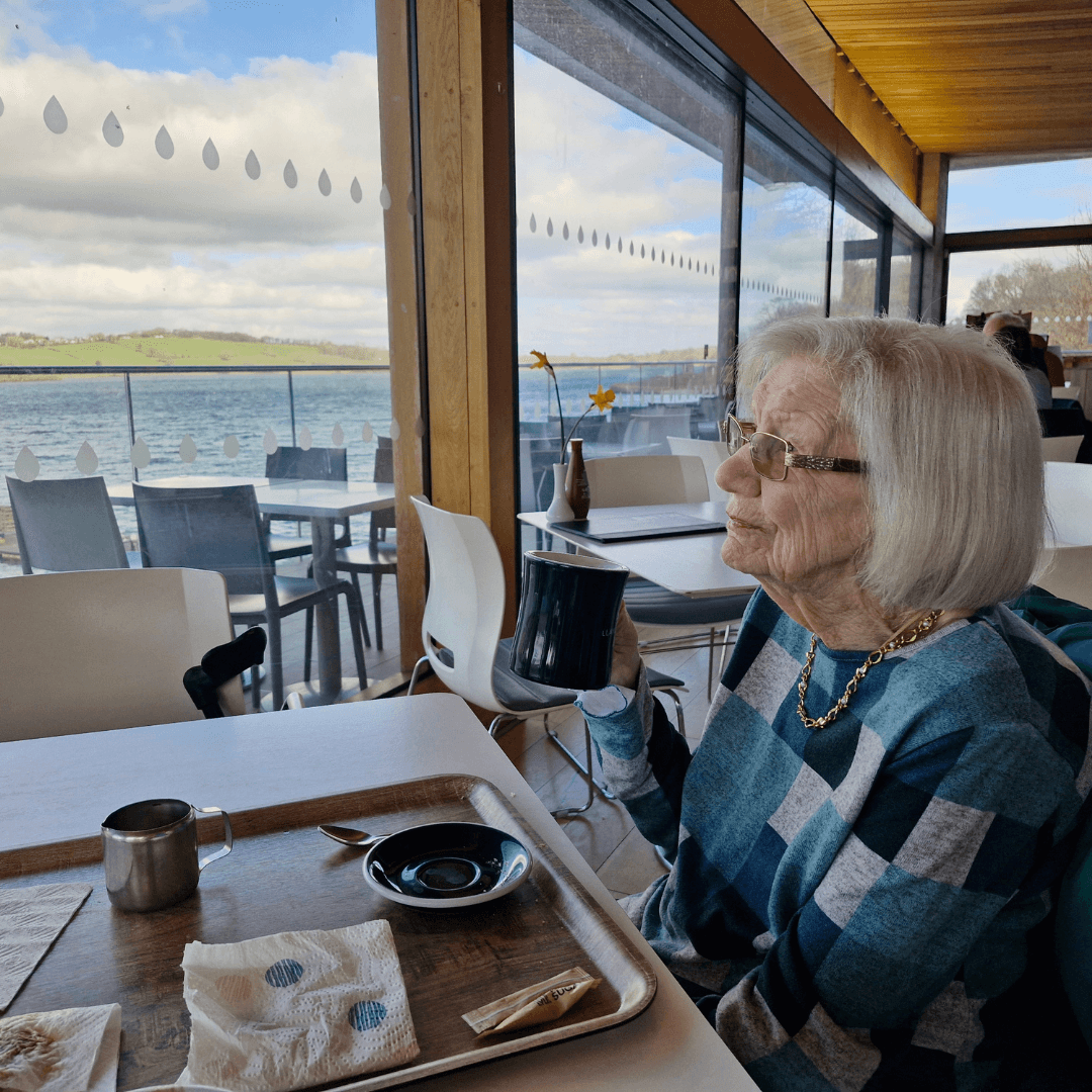 Elderly lady having a cup of tea in a cafe with a lake view