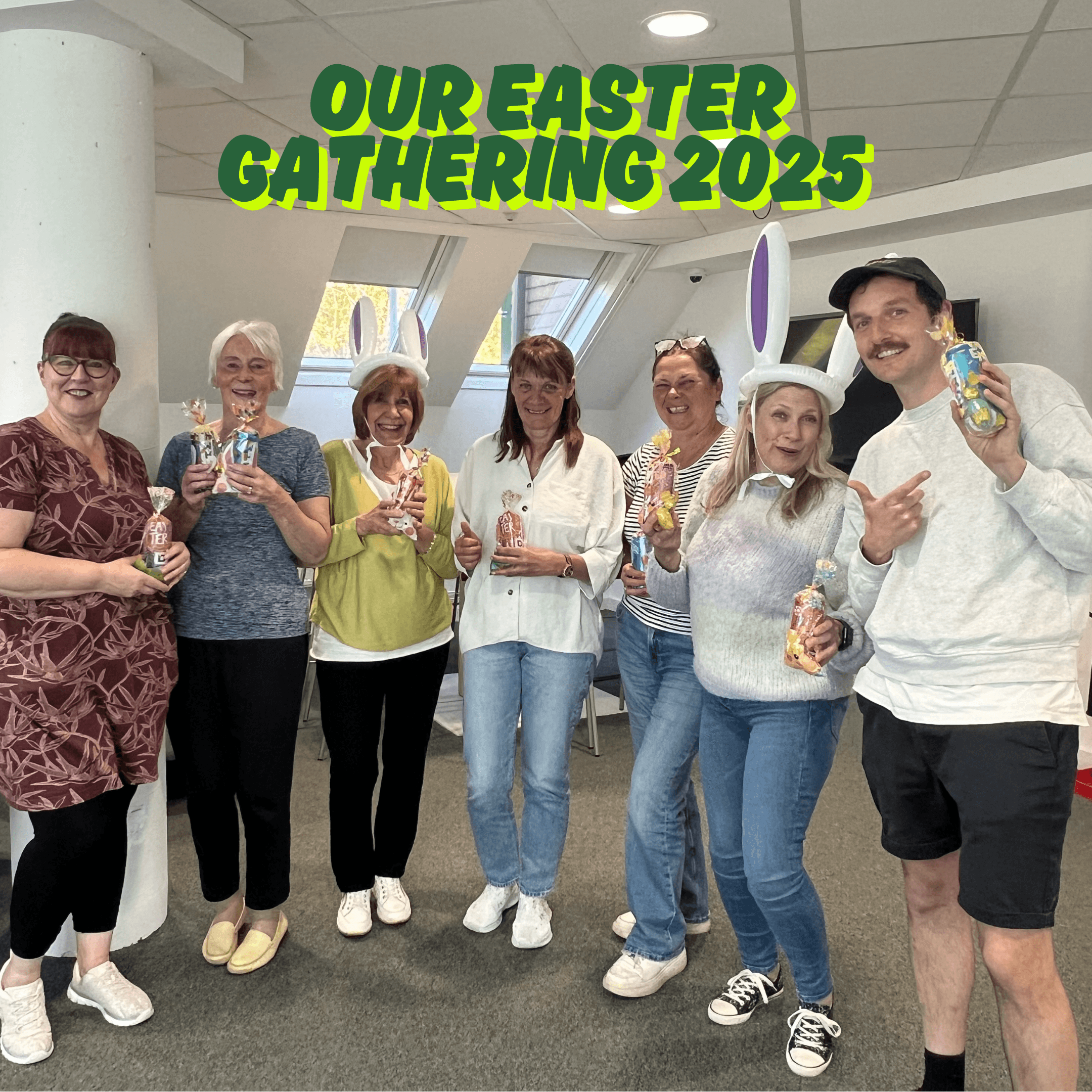 Seven adults smiling and holding drinks at an Easter gathering, with festive text above them. - Home Instead