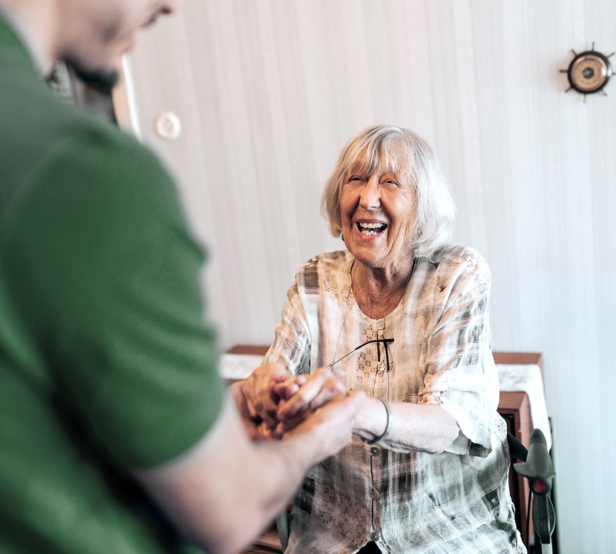 older female adult with grey hair sitting on a wheel chair happy and smiling while being held by her carer