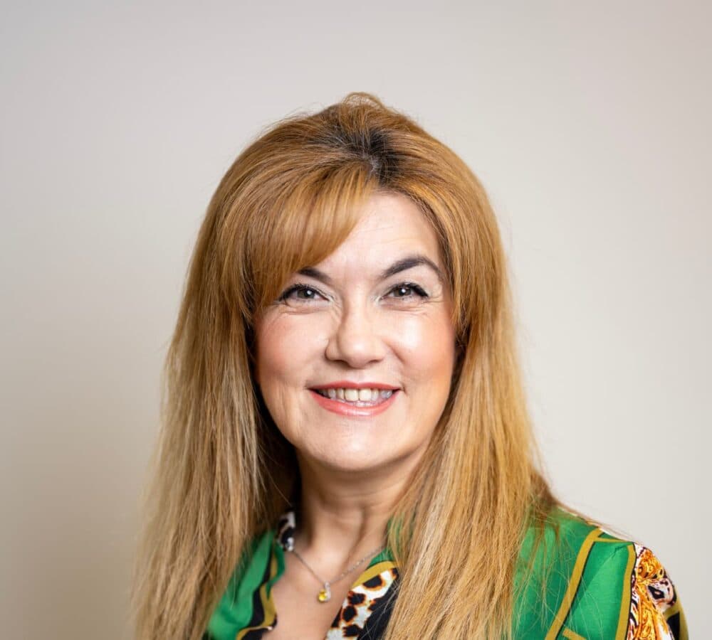 A woman with long light brown hair smiling and wearing green top
