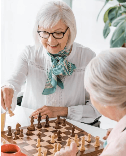 Two elderly women smiling while playing chess at a table indoors. - Home Instead