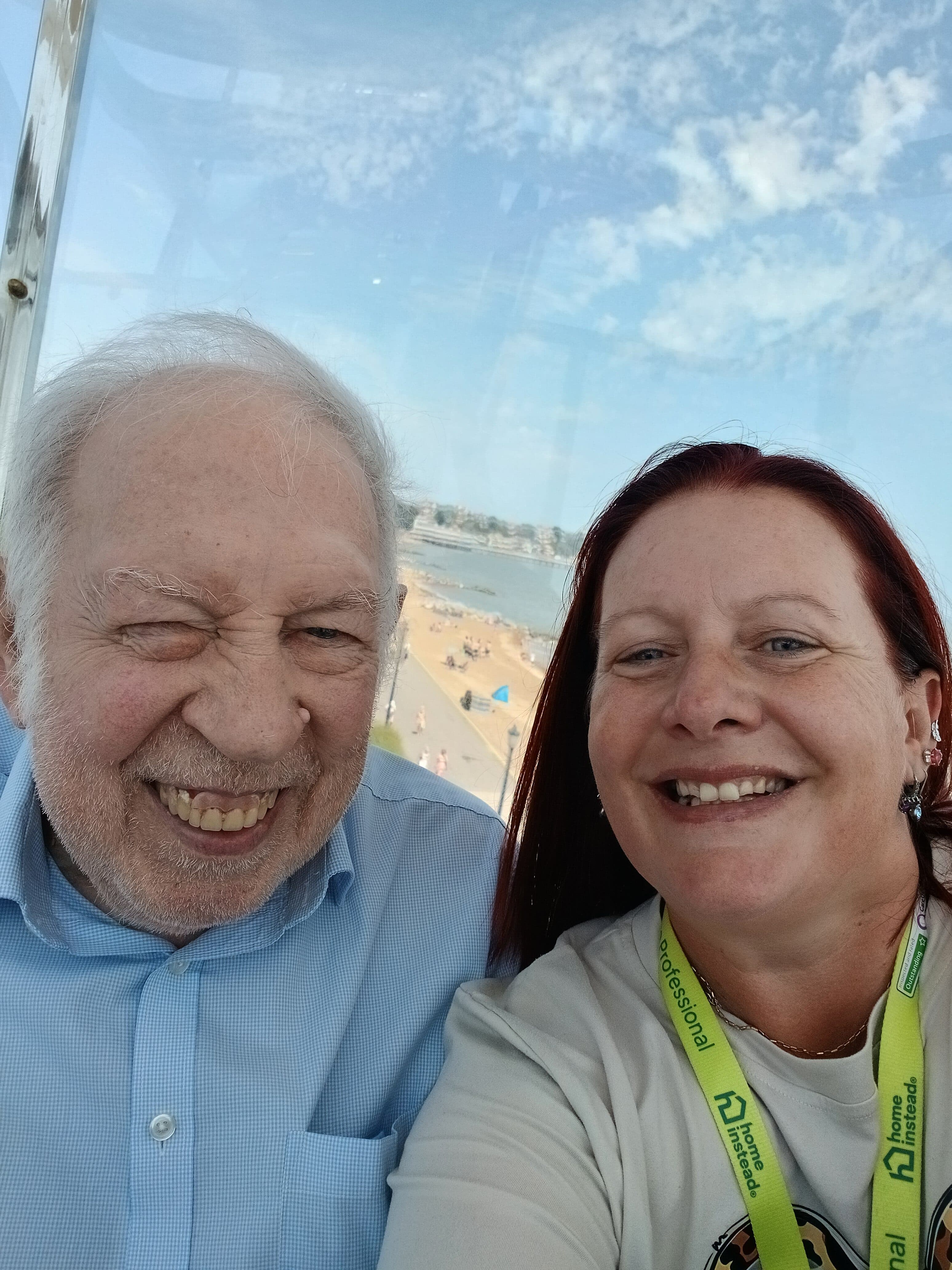 Smiling man and woman taking a selfie with a beach and blue sky in the background. - Home Instead