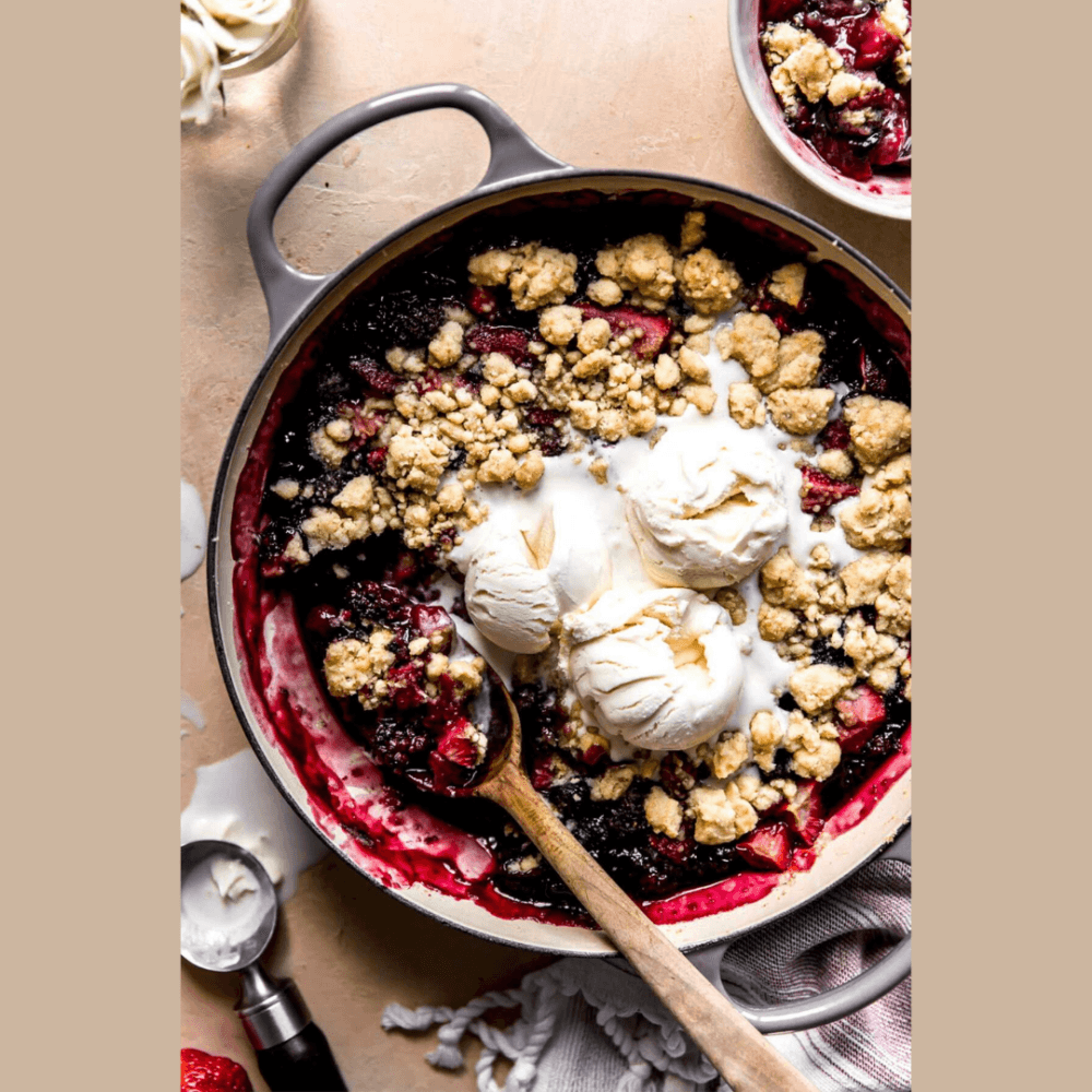 A fruit crumble in a baking dish topped with vanilla ice cream, with a wooden spoon and a bowl nearby. - Home Instead