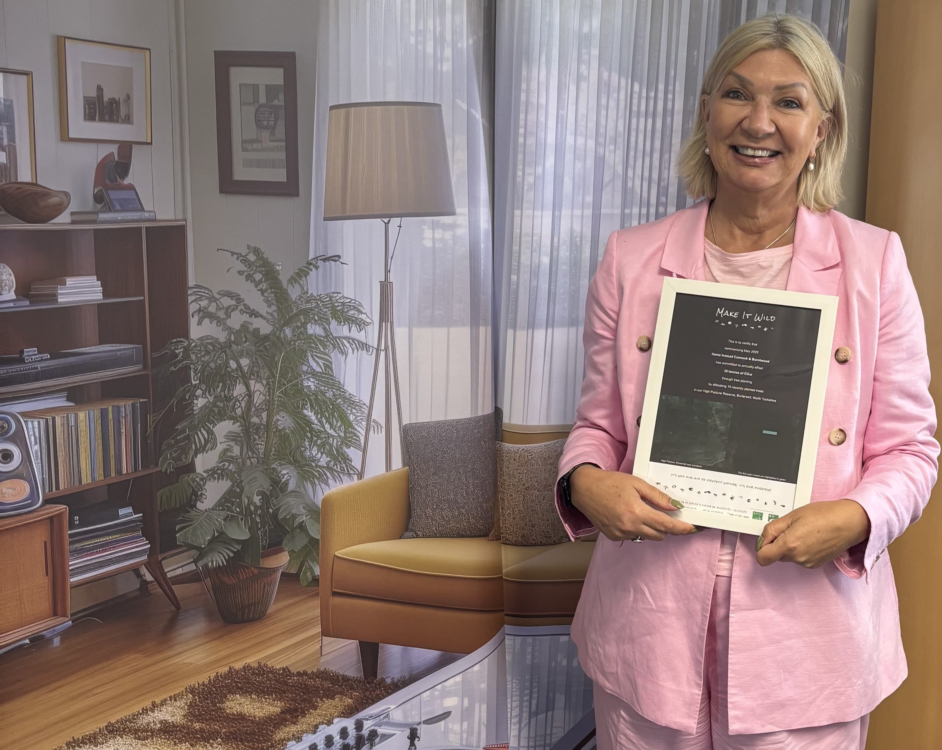 Woman in a pink suit smiling and holding a document, standing in a cozy, retro-styled living room. - Home Instead