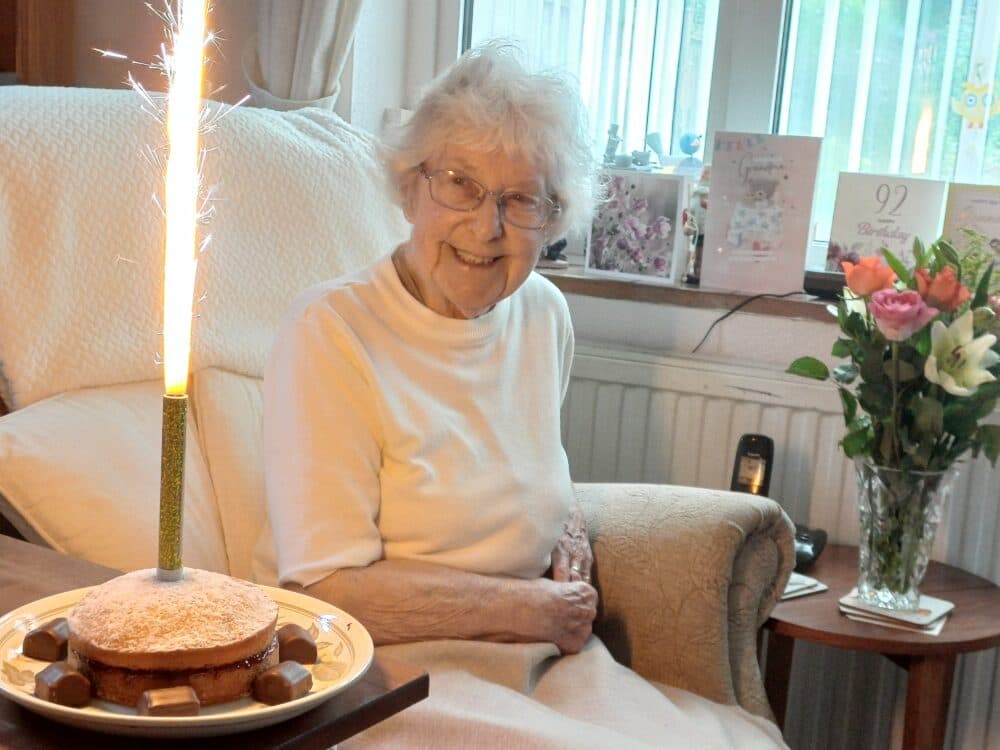 Client PW birthday photo - she is looking at a cake with a candle on it.