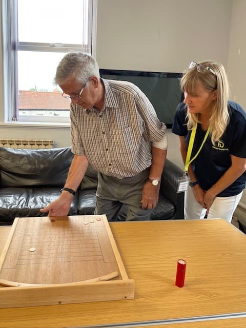 An older man and a woman play a tabletop game with discs in a bright room. - Home Instead