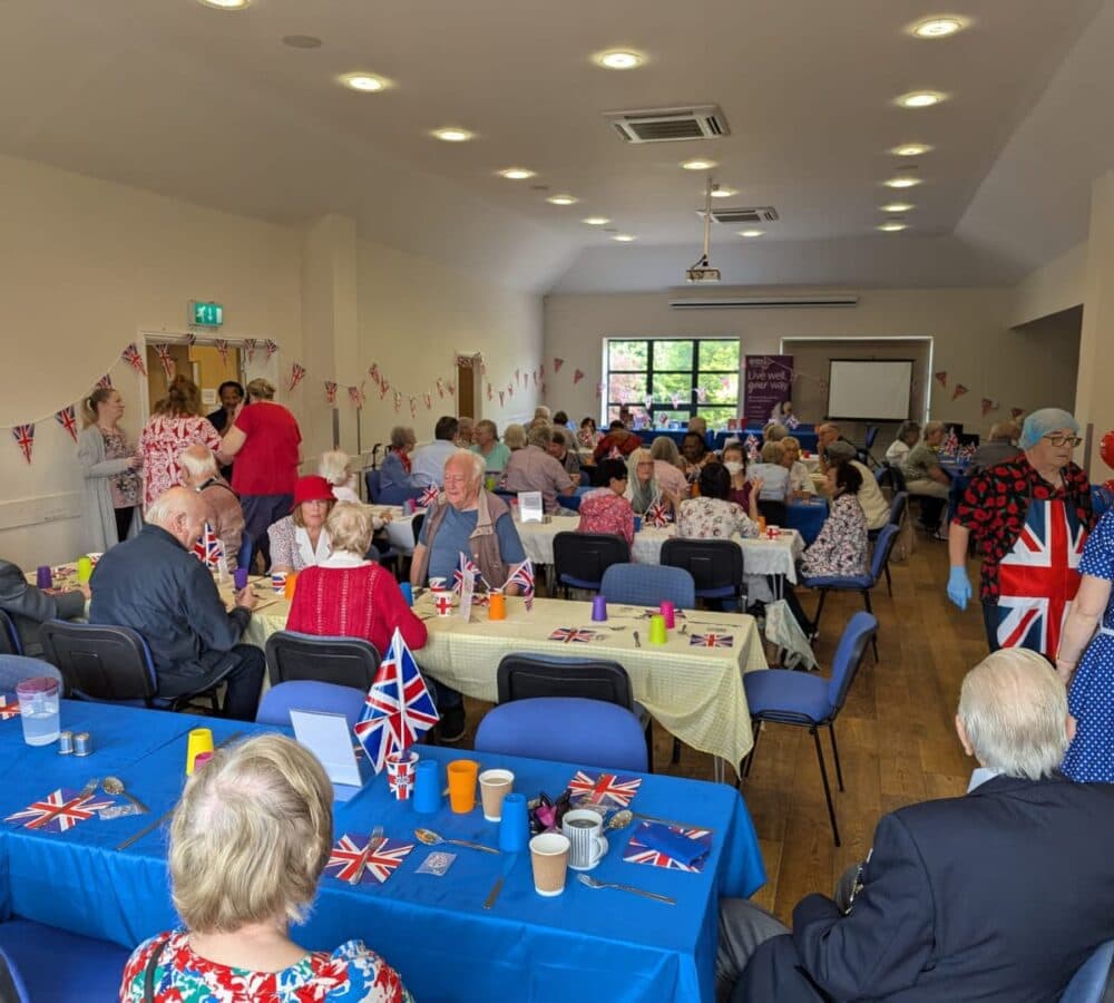 A group of people inside a hall having lunch together with flags and tablecloths and people happy