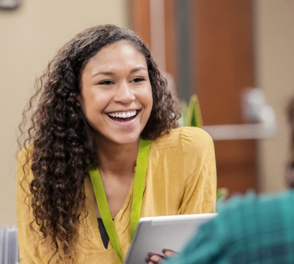 A woman with long curly hair and wearing mustard happy and smiling inside a room