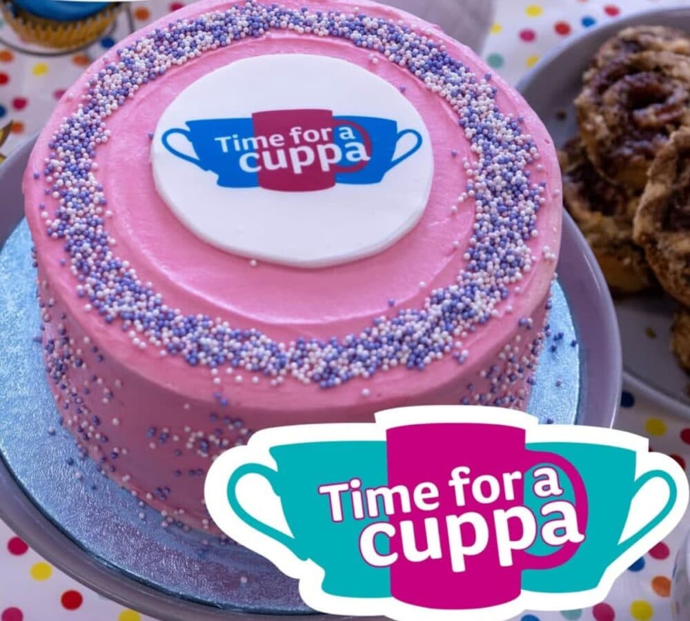 Pink round cake with some sprinkles and with a sign saying time for a cuppa