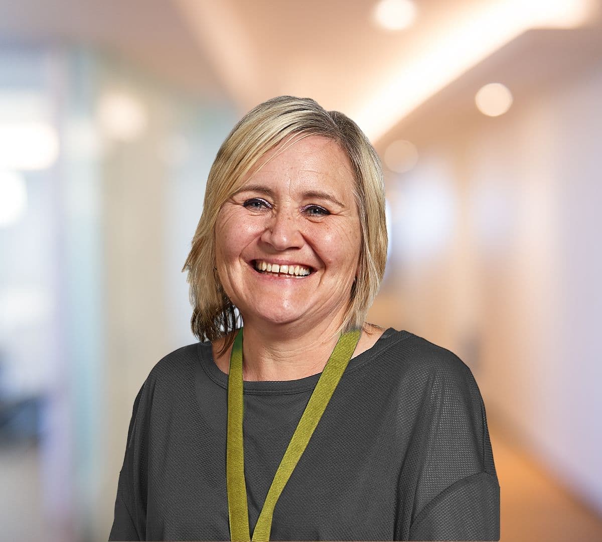 A woman with short blonde hair and wearing green smiling and happy inside the office