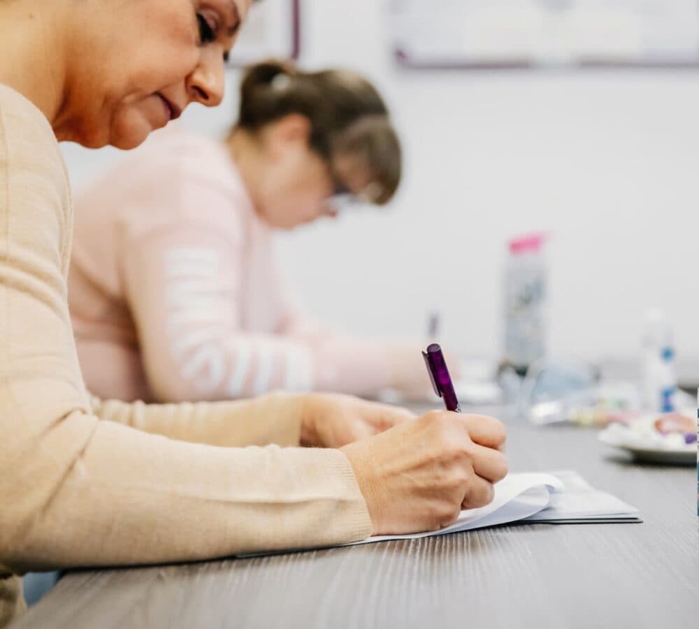 Two women writing on the desk while having training inside a room