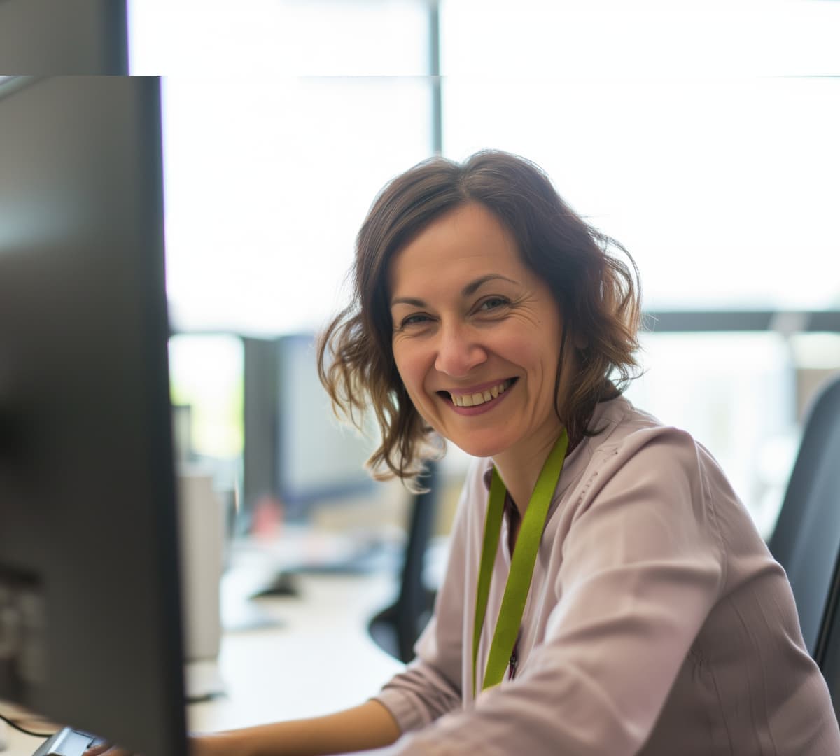 A woman with short curly hair and sitting in front of the computer while smiling