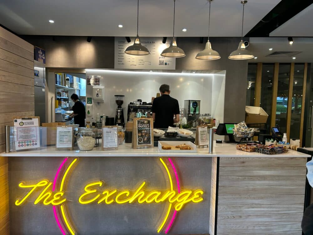 An internal view of The Exchange coffee shop, showing the counter with pastries on display and the barista working behind.