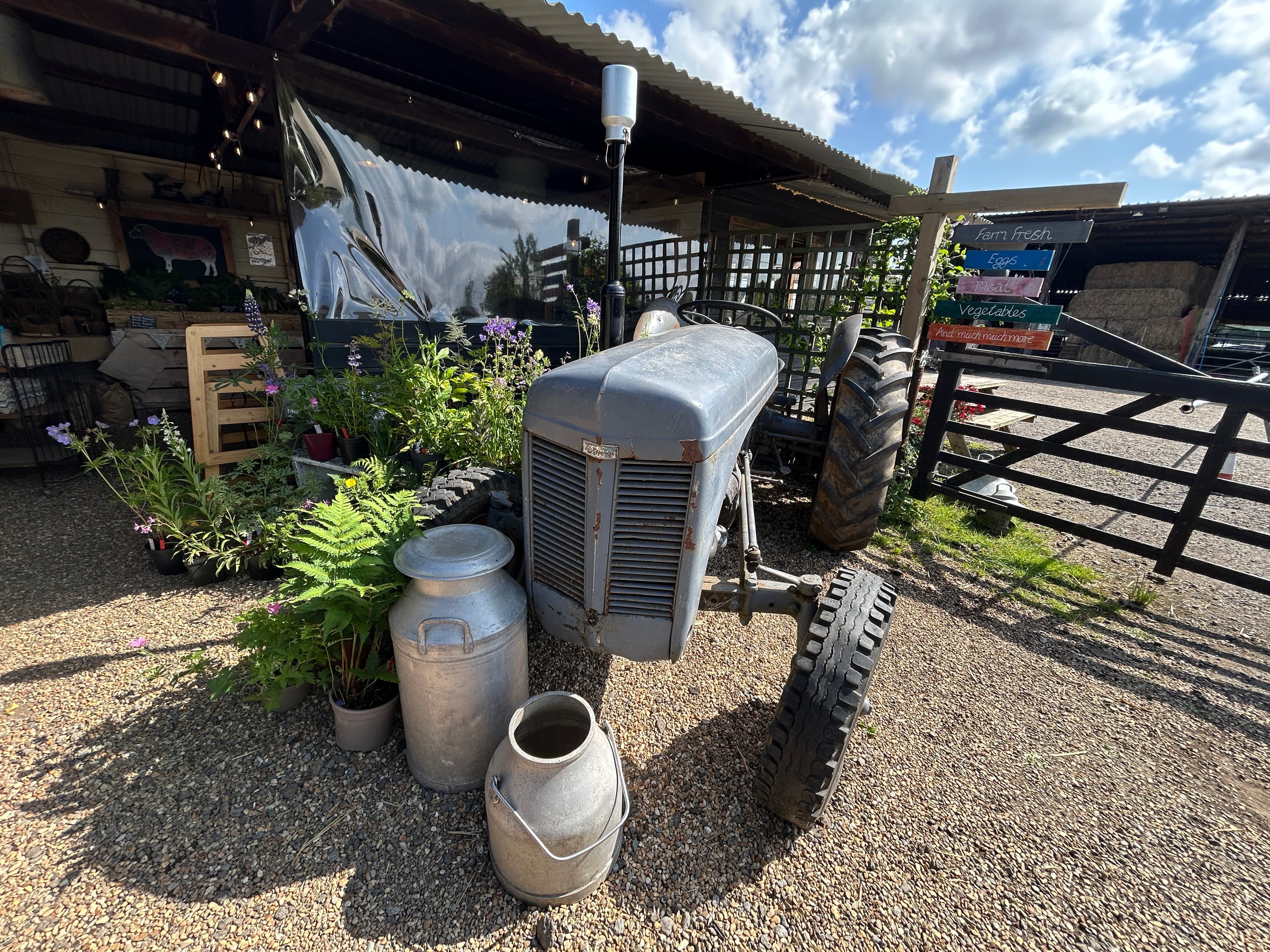 Disused old fashioned farm tractor with milk urns in front and part of the farm shop behind, at Street Croft Farm