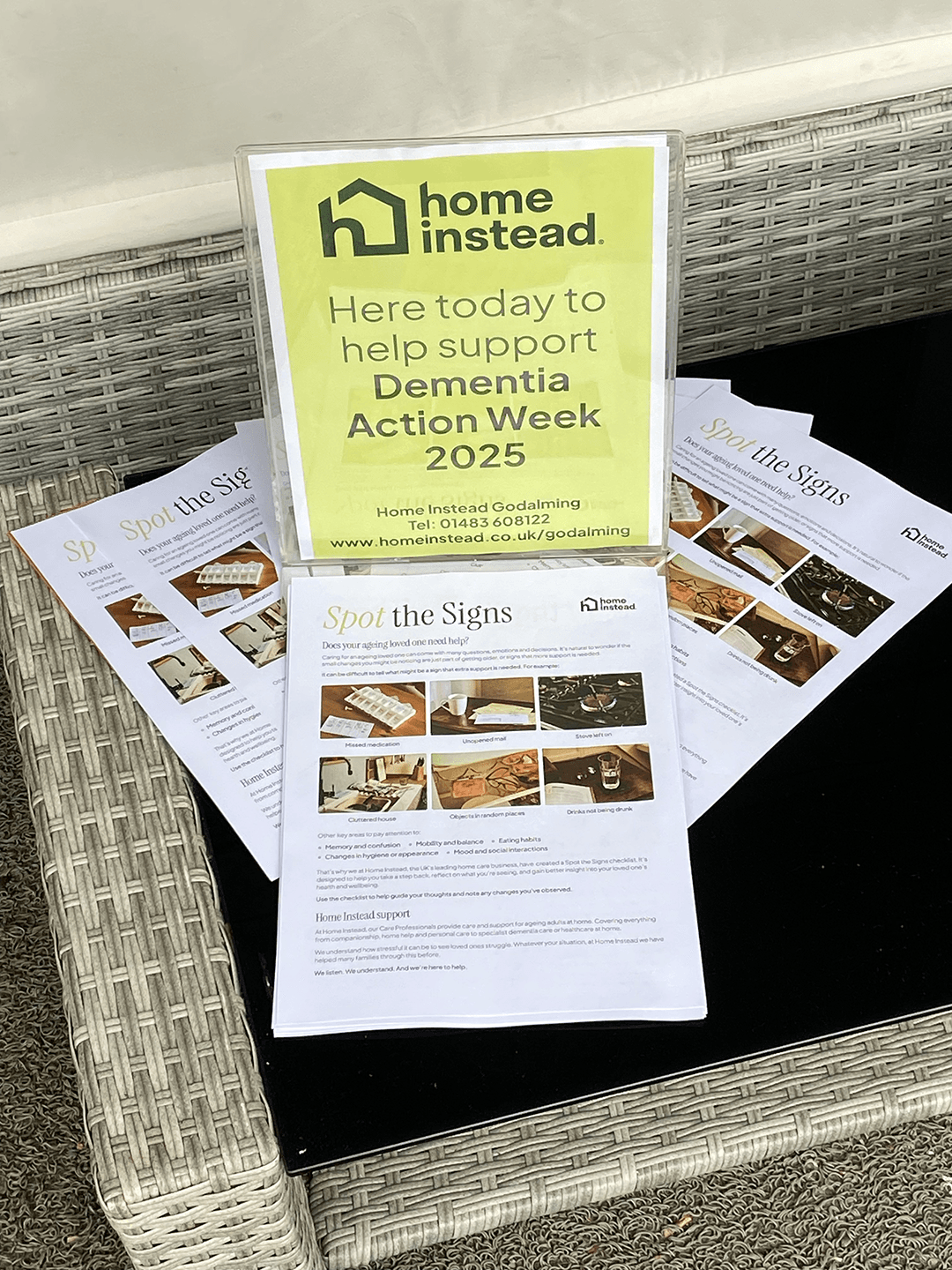 A sign for Dementia Action Week 2025 and leaflets titled "Spot the Signs" on a wicker table. - Home Instead