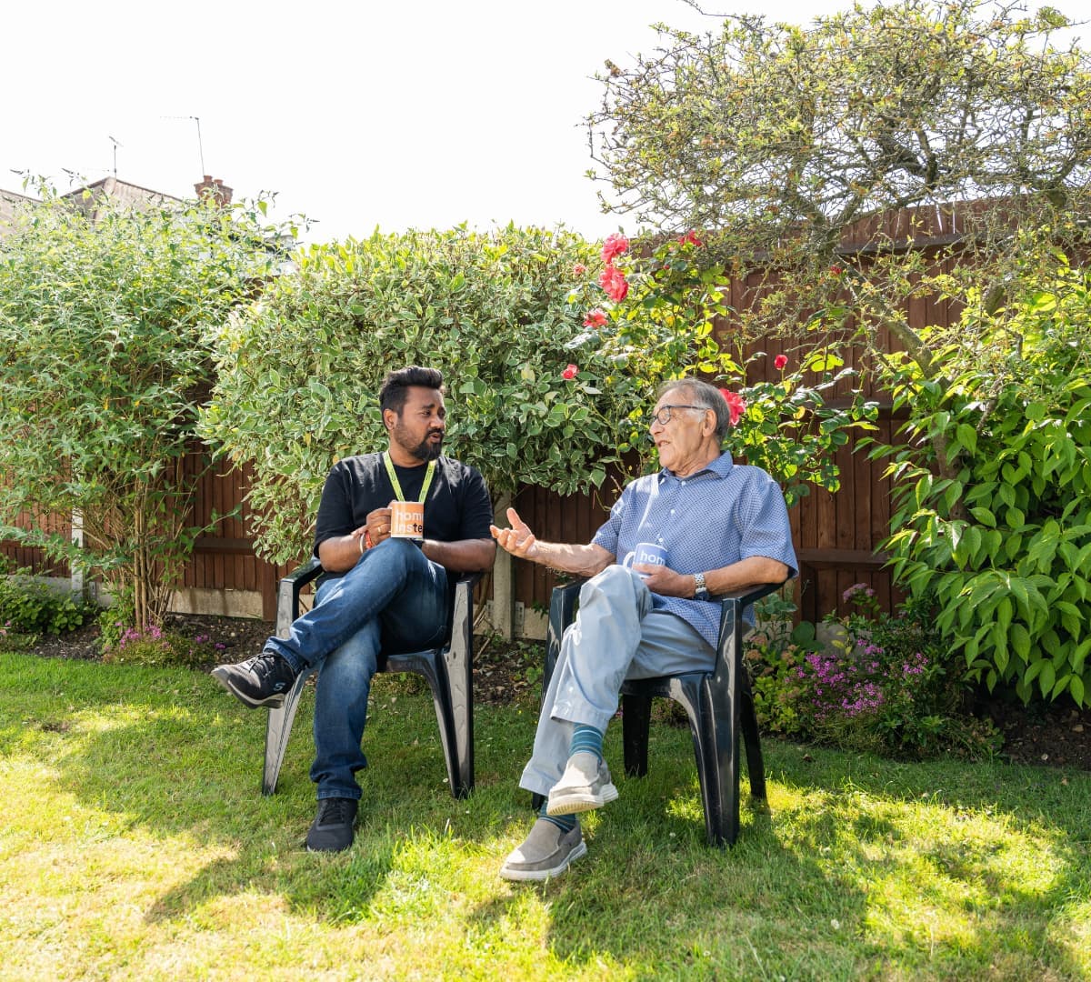 Two men sitting in the garden while drinking coffee using Home Instead mugs and with great sunshine