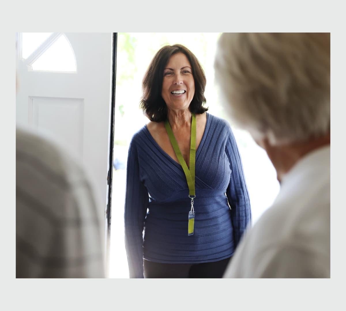 A woman at the door with black hair smiling while wearing blue top while entering the door