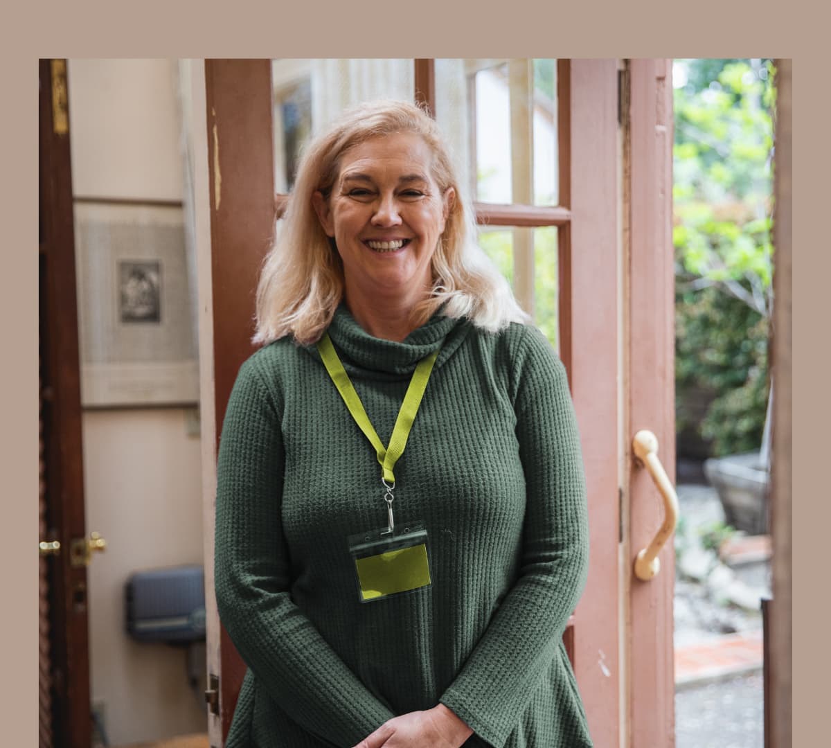 A woman with long blonde hair wearing green standing at the door