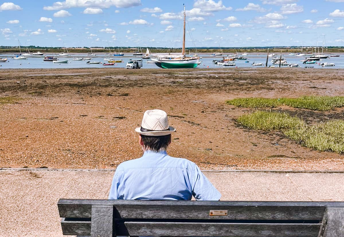 Elderly man sitting on bench enjoying the view of the Essex seaside
