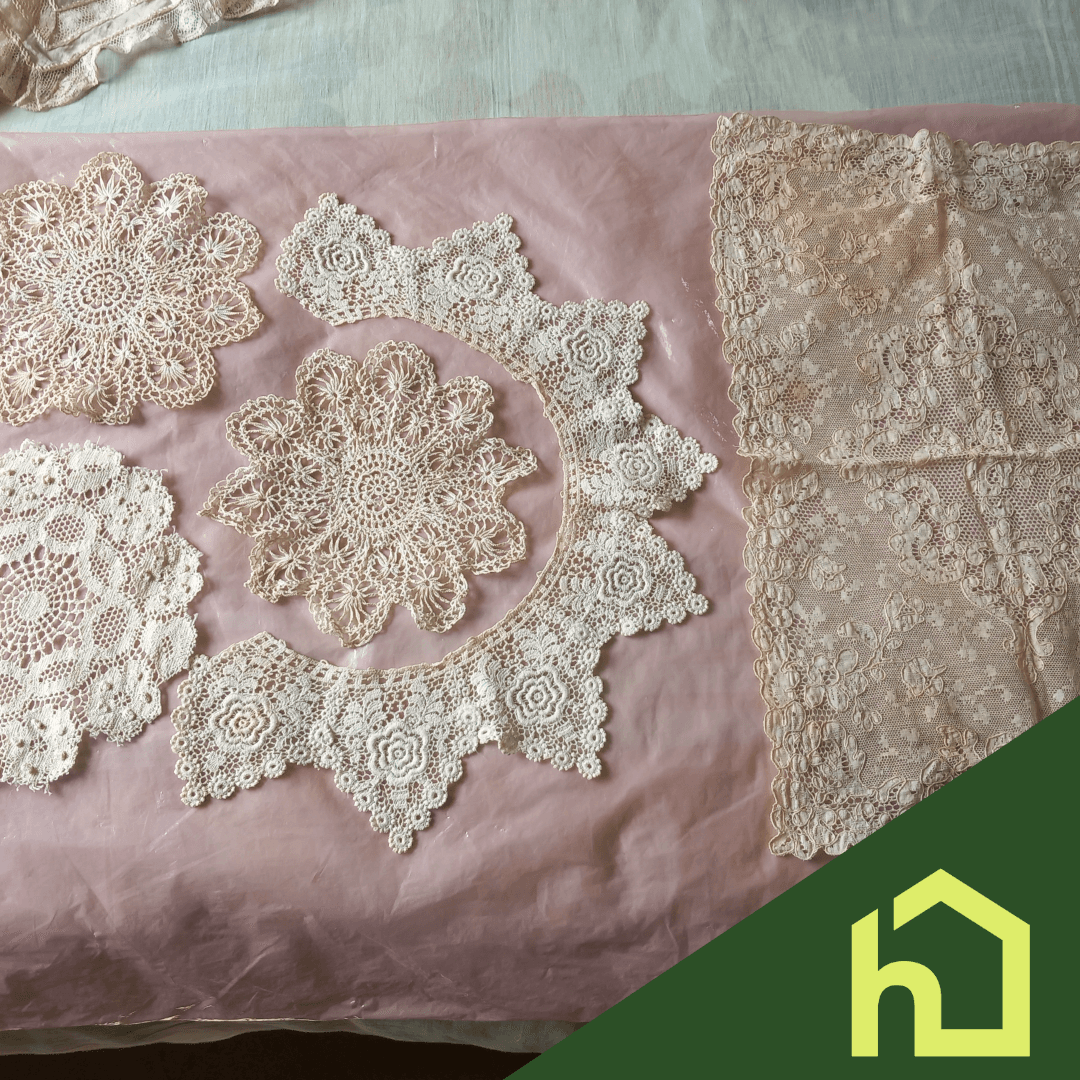 Various lace doilies and a lace fabric are displayed on a pink surface with a green house logo in the corner. - Home Instead
