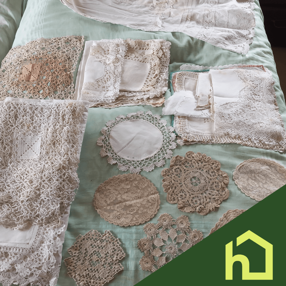 Assorted vintage lace and crocheted doilies arranged on a light green bedspread, with a green house icon. - Home Instead