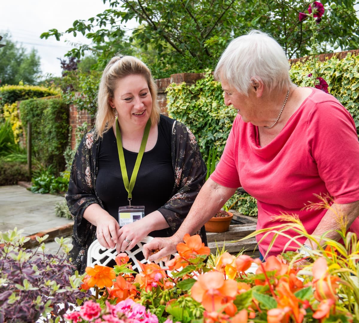An older female adult with grey hair in the garden with her younger female carer