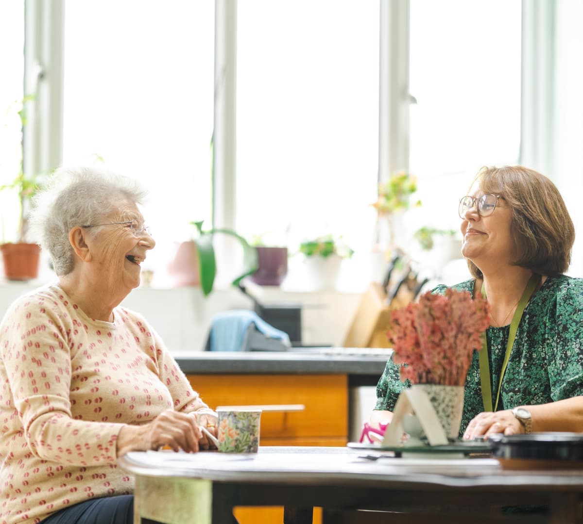 Two women having a cup of tea while chatting and laughing together inside the kitchen