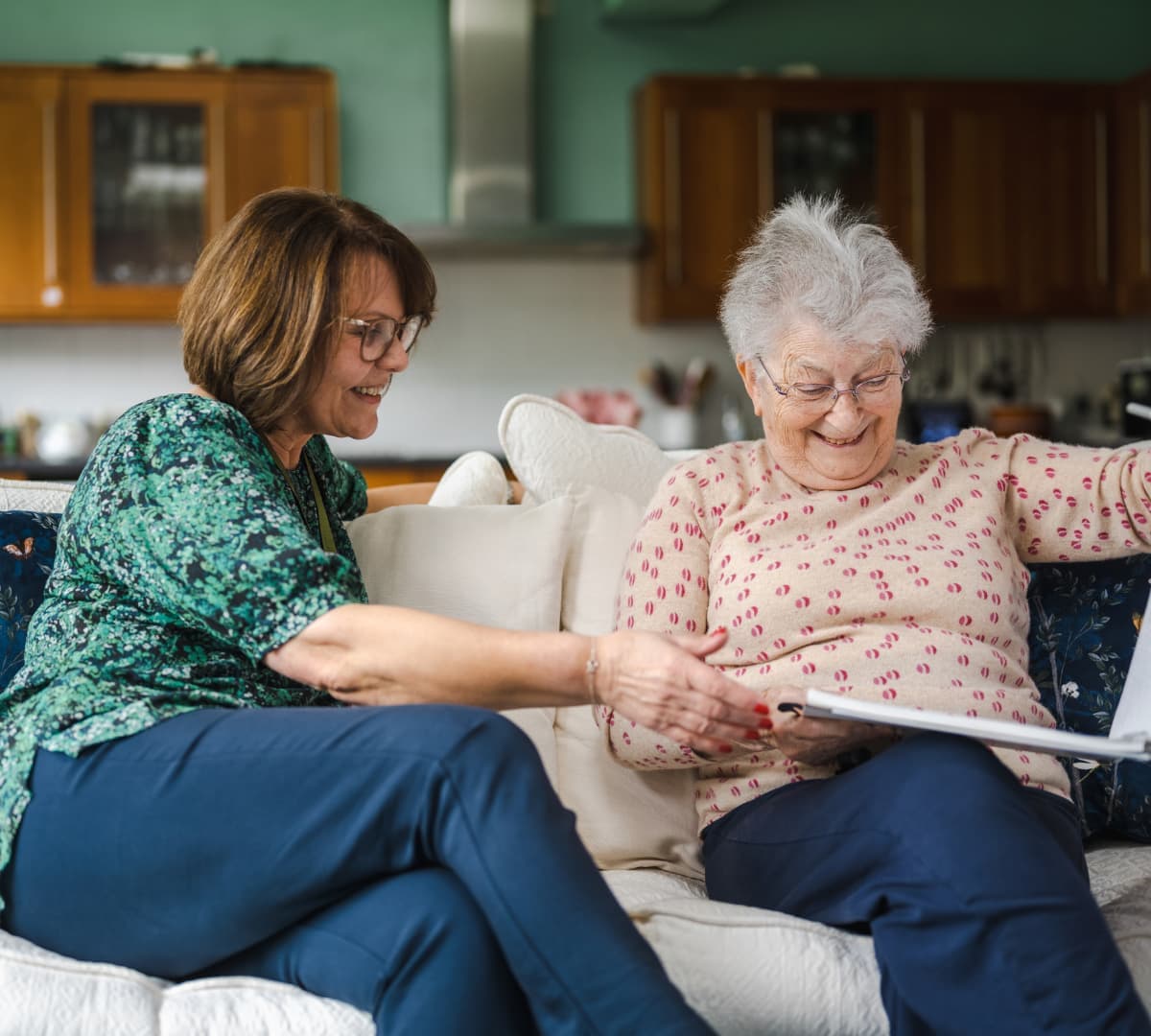 An older female adult looking at a photo album while sitting on a couch with her younger female carer inside the house