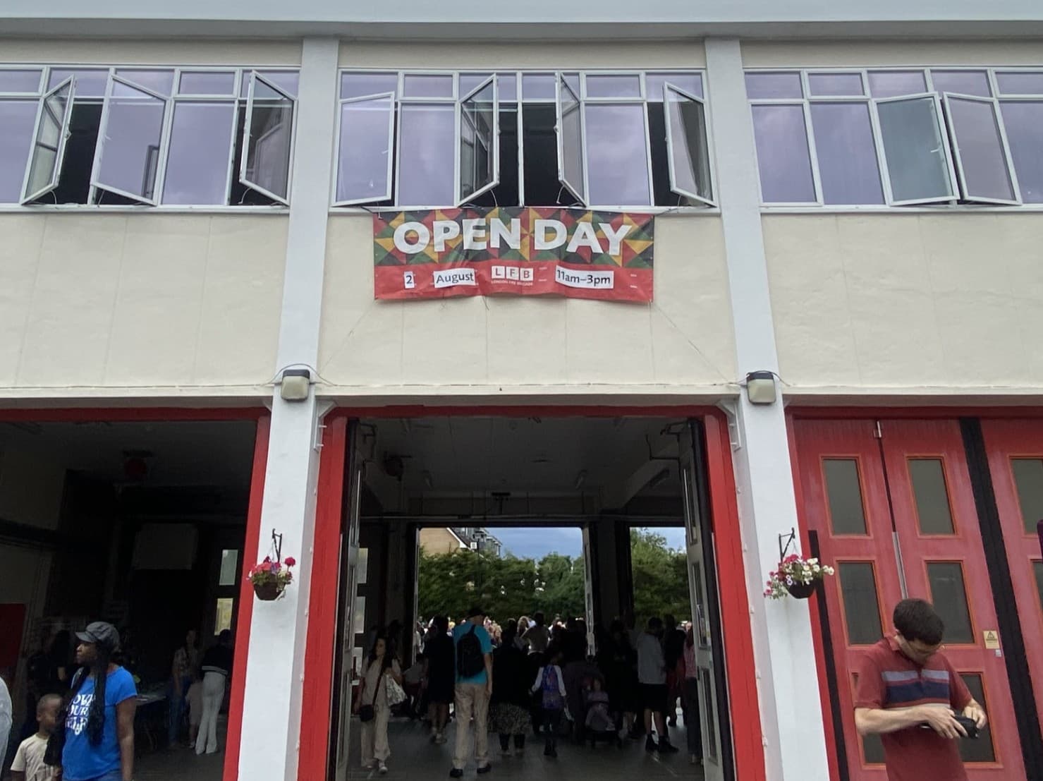 People gather at a building entrance under an "Open Day" banner with red doors and open windows above. - Home Instead