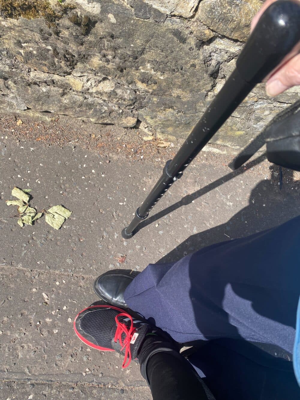 Two people’s feet on a sidewalk; one uses a cane, the other wears black shoes with red laces. - Home Instead