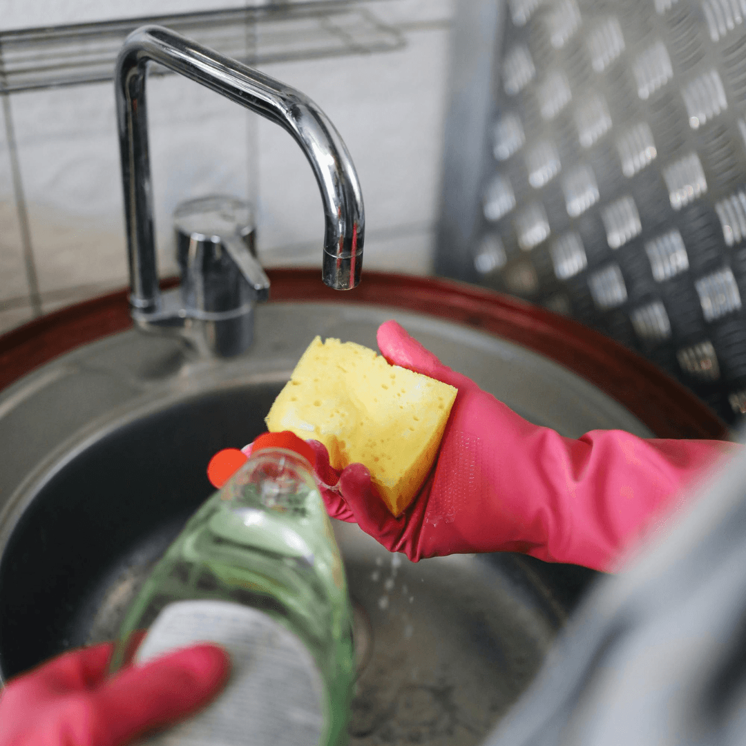 Pink rubber gloves, with a sponge and fairy liquid in the sink
