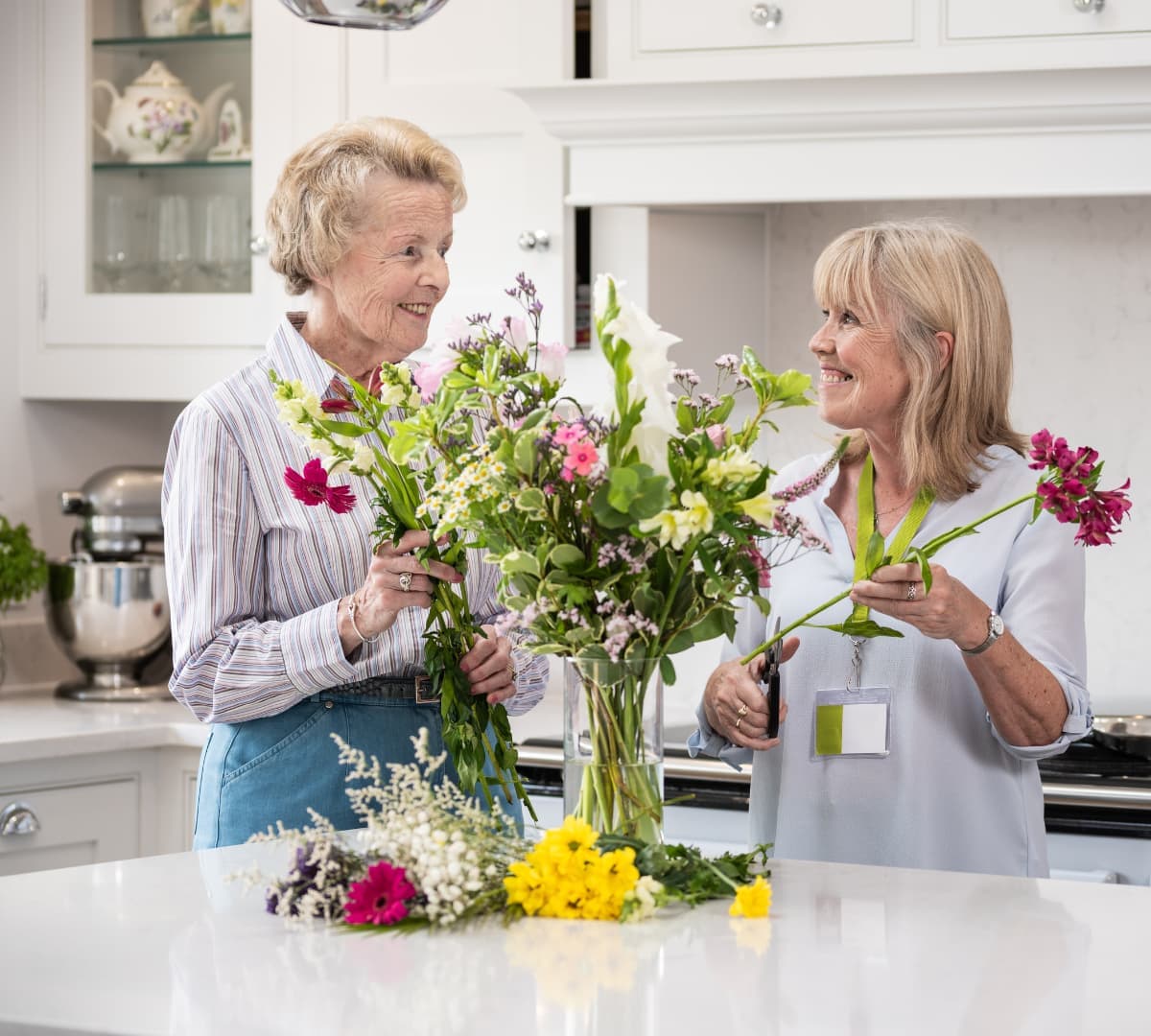 Two women happily arranging flowers and putting it in a vase