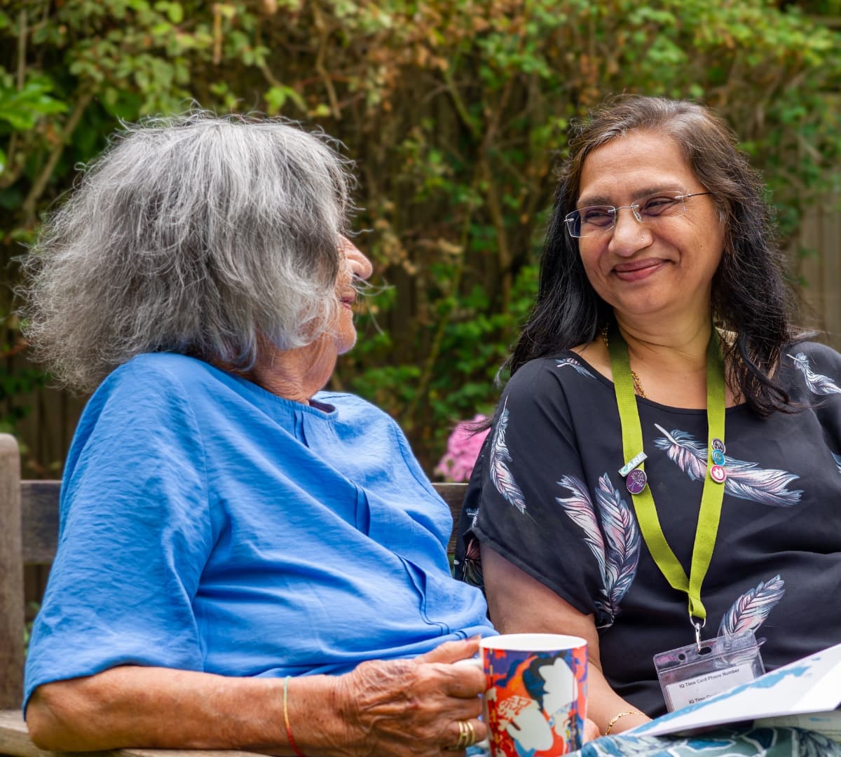 Two women happy and smiling while sitting on a bench in the garden Home Instead