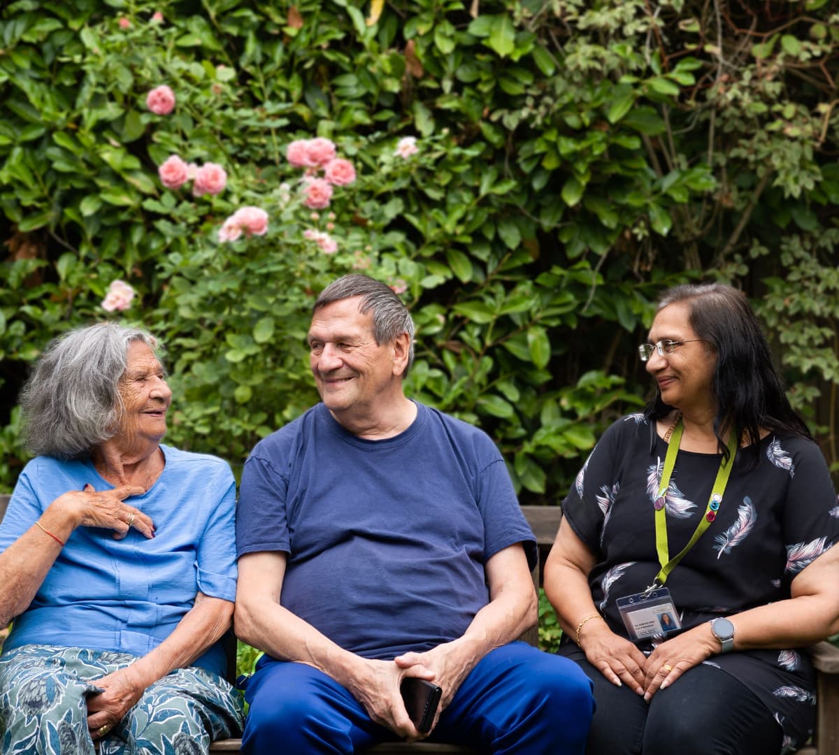 Three people sitting on a bench while happily chatting together inside the garden