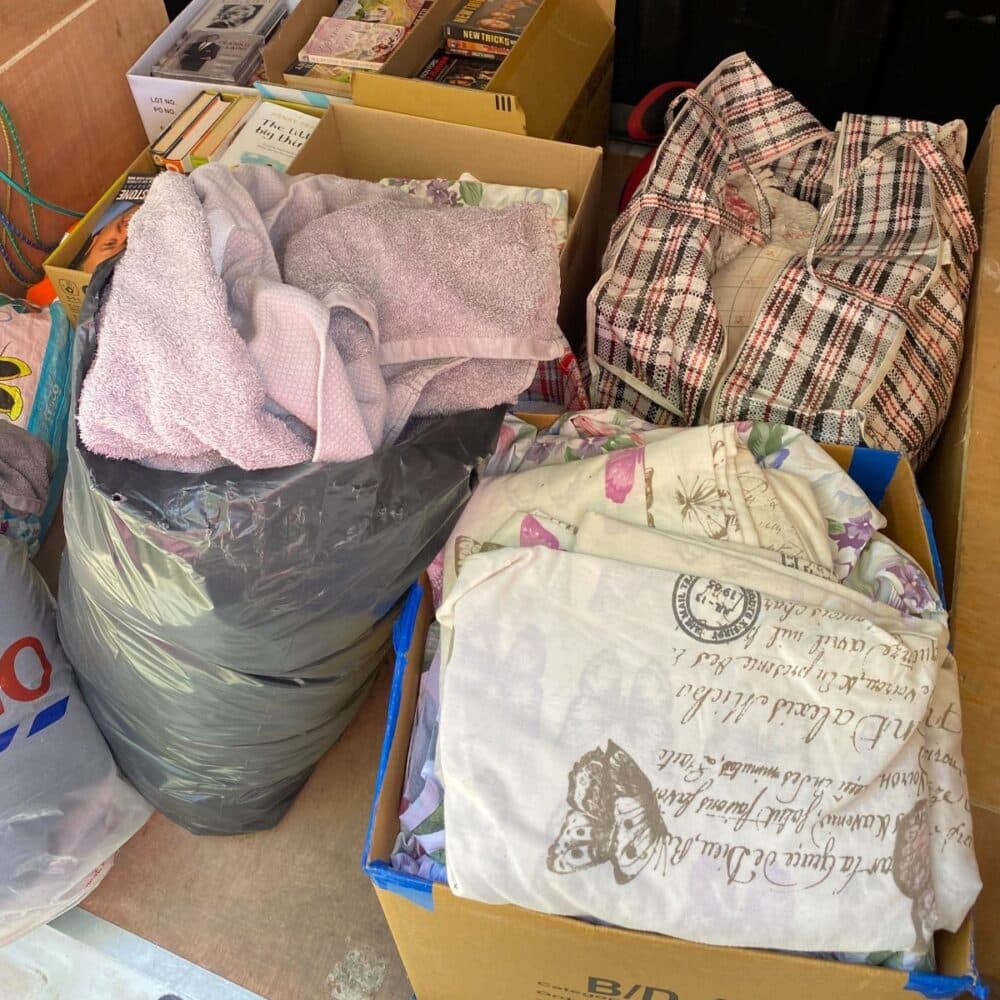 Boxes and bags filled with folded blankets and linens, surrounded by other packed items. - Home Instead