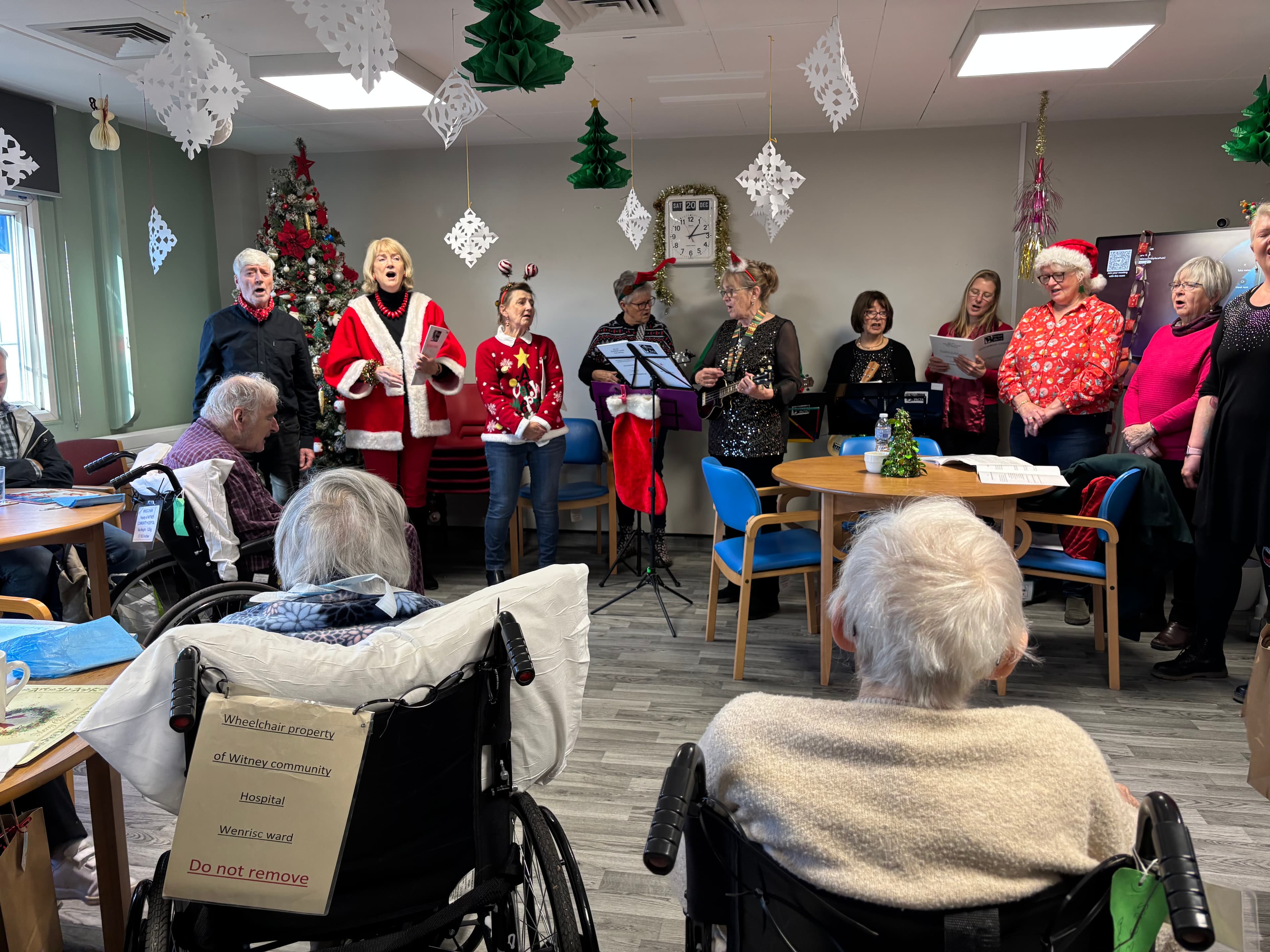 A group sings Christmas carols to elderly people in wheelchairs at a festive, decorated care home. - Home Instead