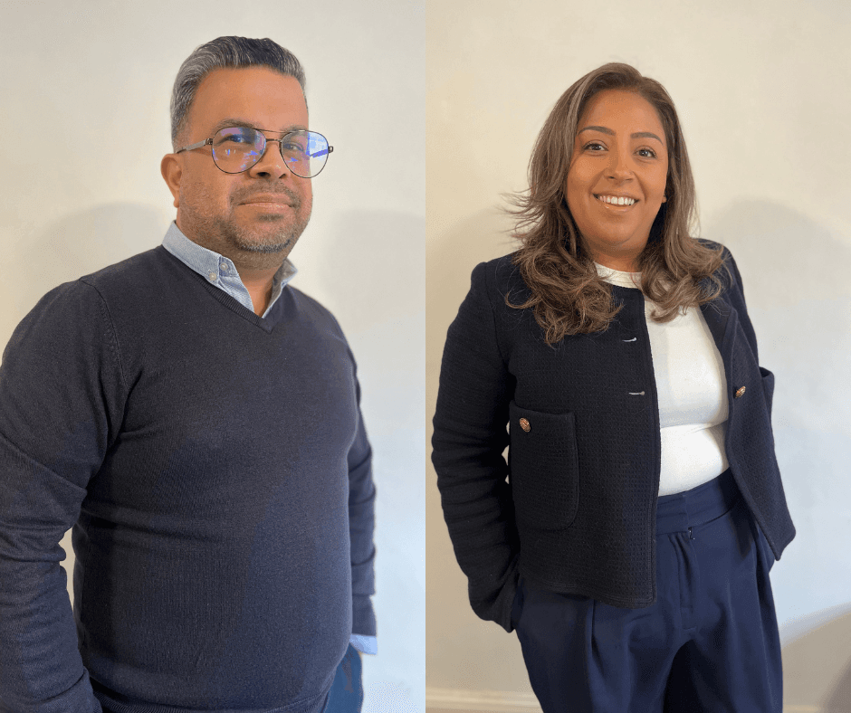 A man with glasses and a woman smile, both wearing dark jumpers and standing against a light background. - Home Instead