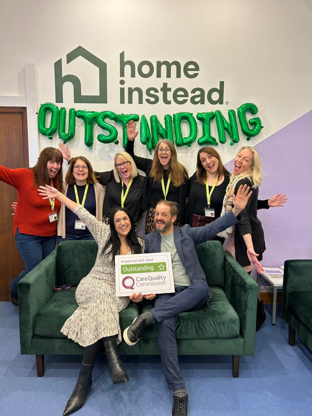 Home Instead team celebrating their Outstanding Care Quality Commission rating with balloons and award sign.