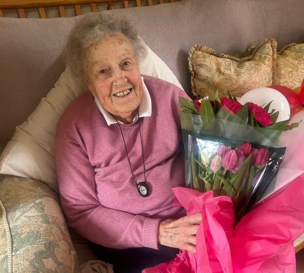 An older female adult with grey hair happy and smiling while sitting on the couch and holding a bouquet of flowers