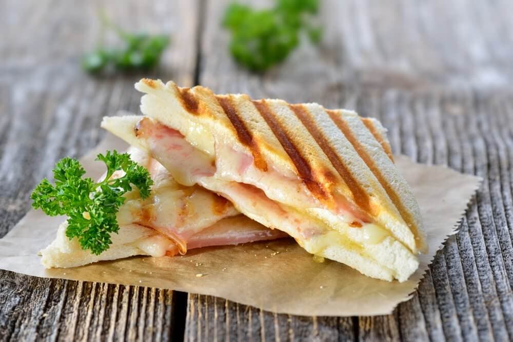 Grilled ham and cheese sandwich on paper, garnished with parsley, on a rustic wooden surface. - Home Instead